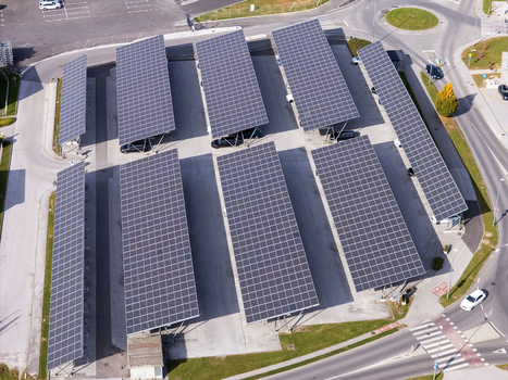 Aerial view of solar panels installed over a parking lot with parked cars and urban infrastructure in Slovenia.