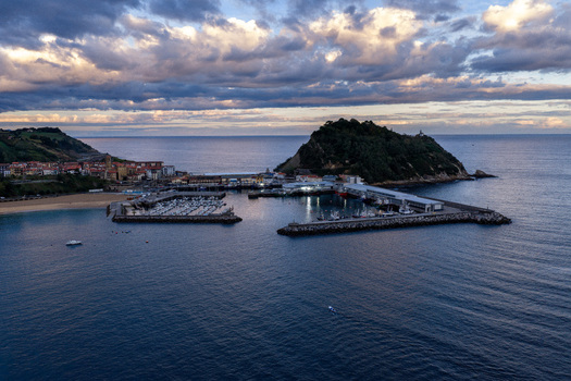 Aerial view of Getariako portua with fishing boats docked in the harbor surrounded by the coastline and the San Anton hill under a cloudy sky in Getaria Basque Country Spain. Aerial view of Getariako portua with fishing boats docked in the harbor surrounded by the coastline and the San Anton hill under a cloudy sky in Getaria Basque Country Spain.