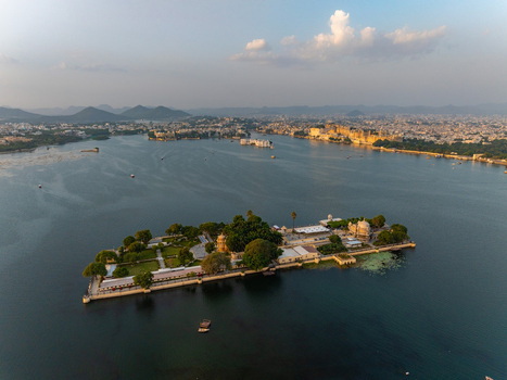 Aerial view of Jag Mandir palace on Lake Pichola surrounded by lush gardens and historic architecture with the city skyline in the background in Udaipur Rajasthan India.