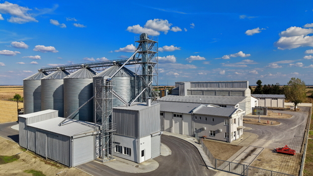 Aerial view of the storage silo facility featuring metallic grain bins industrial buildings and paved roads under a clear blue sky in Bavaniste Vojvodina Serbia.
