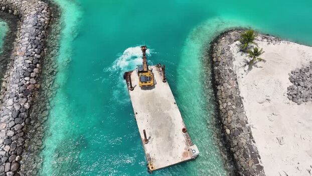 Aerial view of an excavator on a barge in turquoise waters Maldives. Aerial view of an excavator on a barge in turquoise waters Maldives.