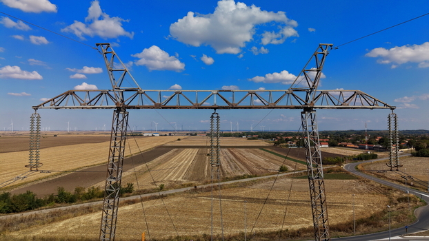 Aerial view of a large metal electric power transmission pylon in a rural landscape with agricultural fields distant wind turbines and a road in Pancevo Serbia.