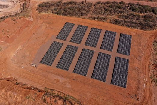 Aerial view of a remote solar energy facility for mining and industrial power featuring rows of photovoltaic panels arranged on arid red earth in Rustenburg North West South Africa.