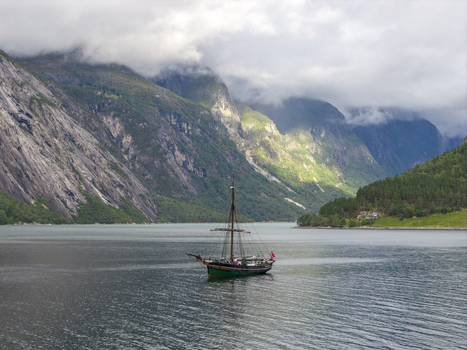 Aerial view of a traditional sailing ship on the Hardangerfjord surrounded by steep mountains and low clouds in Blurnes Vestland Norway. Aerial view of a traditional sailing ship on the Hardangerfjord surrounded by steep mountains and low clouds in Blurnes Vestland Norway.