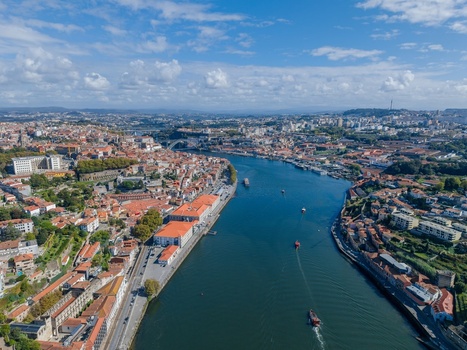 Aerial view of the historic city of Porto along the Douro River featuring traditional red tiled rooftops urban architecture and boats navigating the waterway in Porto Porto District Portugal.