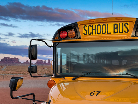 View of a yellow school bus parked in front of the iconic sandstone buttes of Monument Valley Tribal Park under a dramatic sunset sky in Oljato Monument Valley Utah United States.