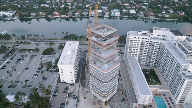 Aerial view of a high rise building under construction with yellow cranes surrounded by residential apartment complexes parking lots and a canal in Miami Beach Florida United States. Aerial view of a high rise building under construction with yellow cranes surrounded by residential apartment complexes parking lots and a canal in Miami Beach Florida United States.