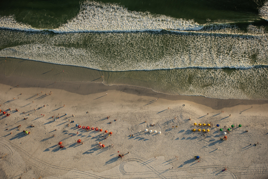 Aerial view of the sandy beach with colorful umbrellas people walking on the sand and gentle waves rolling onto the shore in Rio de Janeiro Rio de Janeiro Brazil. Aerial view of the sandy beach with colorful umbrellas people walking on the sand and gentle waves rolling onto the shore in Rio de Janeiro Rio de Janeiro Brazil.