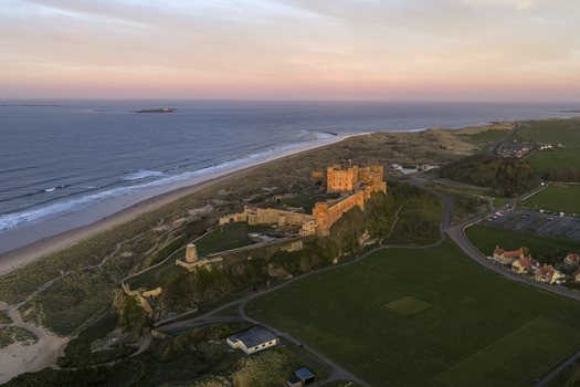 Aerial view of Bamburgh Castle standing on a rocky plateau overlooking the sandy beach and North Sea during a sunset in Bamburgh England United Kingdom. Aerial view of Bamburgh Castle standing on a rocky plateau overlooking the sandy beach and North Sea during a sunset in Bamburgh England United Kingdom.