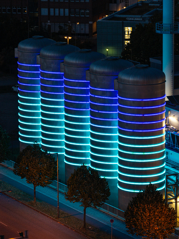 Aerial view of the BTB Heat and Power Plant Adlershof featuring glowing blue and cyan LED rings on industrial storage tanks that visualize real time heat energy in Berlin Berlin Germany. Aerial view of the BTB Heat and Power Plant Adlershof featuring glowing blue and cyan LED rings on industrial storage tanks that visualize real time heat energy in Berlin Berlin Germany.