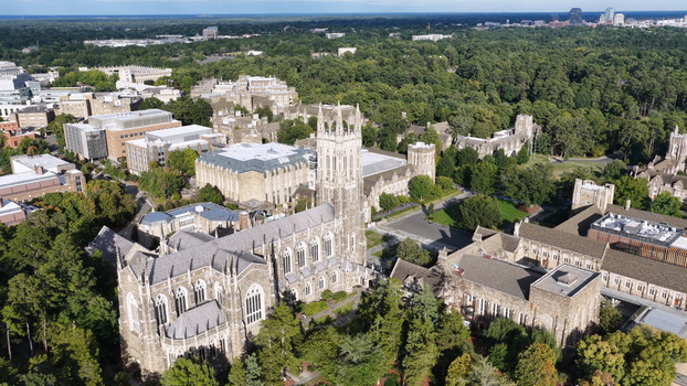 Aerial view of Duke University Chapel surrounded by historic gothic architecture lush green trees and campus buildings in Durham North Carolina United States. Aerial view of Duke University Chapel surrounded by historic gothic architecture lush green trees and campus buildings in Durham North Carolina United States.