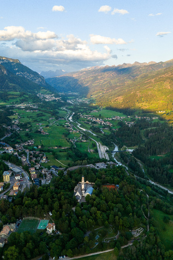 Aerial view of Fiemme Valley featuring a church nestled in lush forests winding river and mountain landscape in Trentino Alto Adige Italy.