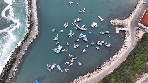 Aerial view of small fishing boats moored in the harbor of Chorrillos with calm turquoise waters rocky breakwaters and a coastal road in Chorrillos Lima Province Peru.