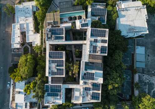 Aerial view of a modern building complex featuring numerous solar panels on the rooftops lush green trees and a swimming pool in Merida Yucatan Mexico. Aerial view of a modern building complex featuring numerous solar panels on the rooftops lush green trees and a swimming pool in Merida Yucatan Mexico.