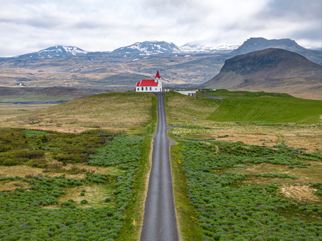 Aerial view of Ingjaldsholl church with its distinctive red roof situated on a hill at the end of a long road surrounded by green fields and mountains in Iceland. Aerial view of Ingjaldsholl church with its distinctive red roof situated on a hill at the end of a long road surrounded by green fields and mountains in Iceland.