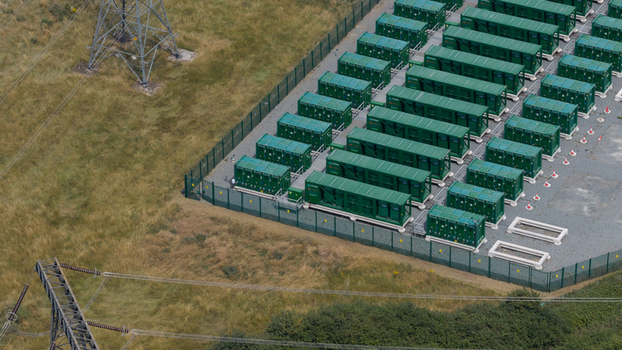 Aerial view of the Thurrock Flexible Generation Substation with rows of green battery storage containers in a fenced compound near power lines in Tilbury England United Kingdom.