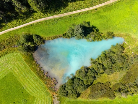 Aerial view of a vibrant turquoise pond surrounded by lush green meadows and dense trees in Sulden Trentino Alto Adige Italy. Aerial view of a vibrant turquoise pond surrounded by lush green meadows and dense trees in Sulden Trentino Alto Adige Italy.
