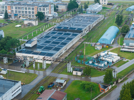 Olaine parish Latvia 04 July 2026 Aerial view of an industrial complex with large factory buildings storage tanks and a small green locomotive on tracks amidst green lawns. Olaine parish Latvia 04 July 2026 Aerial view of an industrial complex with large factory buildings storage tanks and a small green locomotive on tracks amidst green lawns.