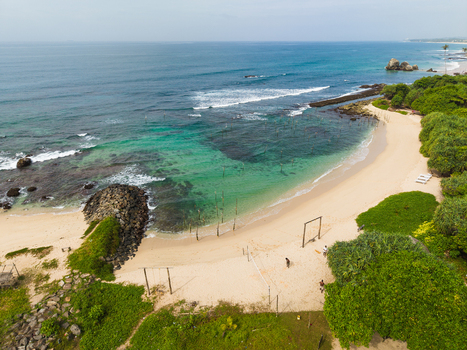 Aerial view of the sandy beach and turquoise waters with traditional stilt fishing poles and lush tropical vegetation in Koggala Southern Province Sri Lanka. Aerial view of the sandy beach and turquoise waters with traditional stilt fishing poles and lush tropical vegetation in Koggala Southern Province Sri Lanka.
