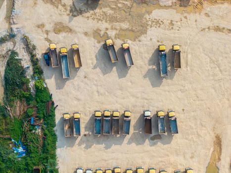 Aerial view of a construction area with rows of yellow dump trucks parked on a dirt lot near green vegetation in Bukit Tambun Penang Malaysia. Aerial view of a construction area with rows of yellow dump trucks parked on a dirt lot near green vegetation in Bukit Tambun Penang Malaysia.