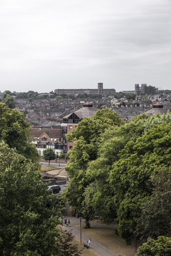Aerial view of the historic city of York featuring dense residential rooftops lush green trees and a pathway with people walking in York England United Kingdom.
