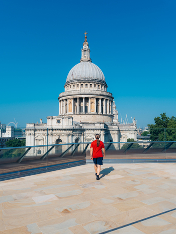 View of a person in a vibrant red shirt walking across a sun drenched rooftop towards the majestic St Paul s Cathedral London England United Kingdom. View of a person in a vibrant red shirt walking across a sun drenched rooftop towards the majestic St Paul s Cathedral London England United Kingdom.