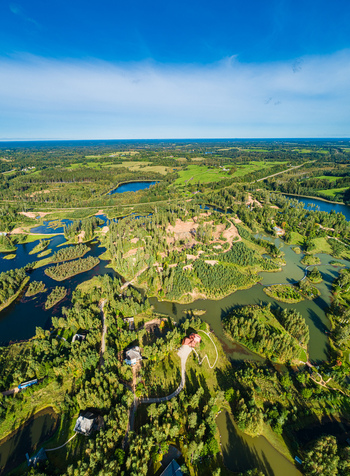 Aerial view of a lush green landscape featuring numerous small lakes dense forests and winding paths under a clear blue sky in Latvia. Aerial view of a lush green landscape featuring numerous small lakes dense forests and winding paths under a clear blue sky in Latvia.