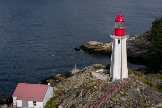 Aerial view of Point Atkinson Lighthouse with its red lantern room and white tower on a rocky coastline overlooking the Pacific Ocean in West Vancouver British Columbia Canada.