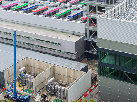 Aerial view of a data center featuring colorful rooftop cooling units modern industrial architecture and a construction site with a blue crane in the United Kingdom.