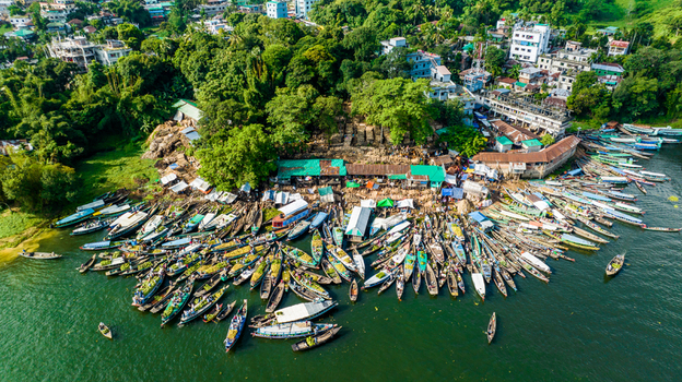 Rangamati Chittagong Bangladesh 19 October 2022 Aerial view of a boat market on Kaptai Lake with wooden boats docked along the waterfront near lush hills and buildings.