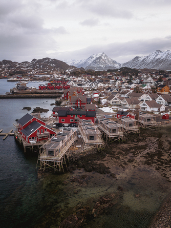 Aerial view of rustic red cabins contrast against the muted landscape nestled by the tranquil waters of the harbor Ballstad Nordland Norway. Aerial view of rustic red cabins contrast against the muted landscape nestled by the tranquil waters of the harbor Ballstad Nordland Norway.