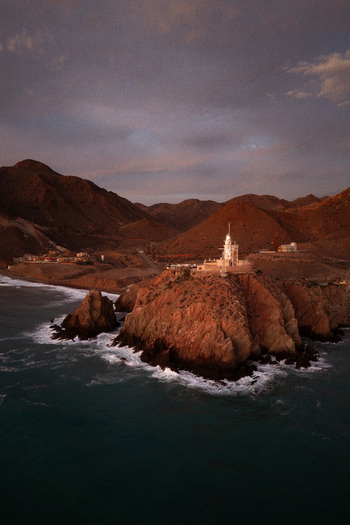 Aerial view of Lighthouse de Cabo de Gata on a rugged cliff overlooking the Mediterranean Sea at sunset with rocky mountains in the background in San Jose Andalucia Spain. Aerial view of Lighthouse de Cabo de Gata on a rugged cliff overlooking the Mediterranean Sea at sunset with rocky mountains in the background in San Jose Andalucia Spain.