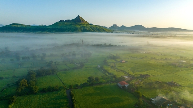 Aerial view of the lush green landscape featuring rolling hills misty fields and small rural houses under a clear morning sky in Igatpuri Maharashtra India.