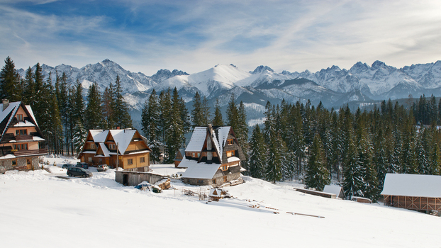View of traditional wooden houses in a snowy landscape with the snow capped peaks of the Tatra Mountains under a blue sky Tatra County Lesser Poland Voivode Poland. View of traditional wooden houses in a snowy landscape with the snow capped peaks of the Tatra Mountains under a blue sky Tatra County Lesser Poland Voivode Poland.