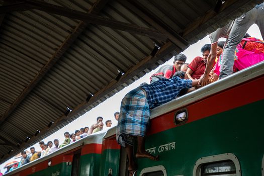 Dhaka Bangladesh 14 June 2018 View of people climbing onto the roof of a crowded green and red train at Airport Railway Station under a corrugated metal roof. Dhaka Bangladesh 14 June 2018 View of people climbing onto the roof of a crowded green and red train at Airport Railway Station under a corrugated metal roof.