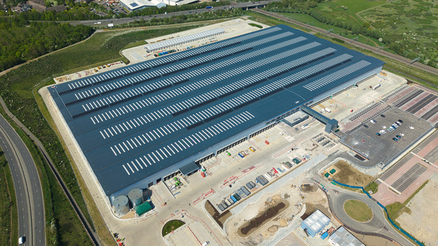 Aerial view of the large Symmetry Park distribution center with solar panels on the roof and surrounding parking areas near the A14 road in Kettering England United Kingdom. Aerial view of the large Symmetry Park distribution center with solar panels on the roof and surrounding parking areas near the A14 road in Kettering England United Kingdom.