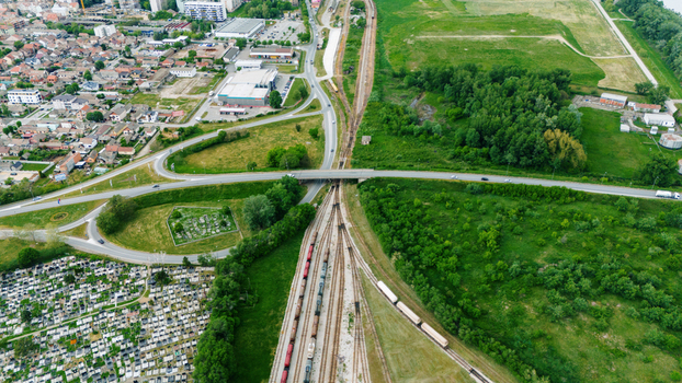 Aerial view of a road interchange crossing over railway tracks with freight trains near a cemetery and urban buildings in Sabac Serbia.