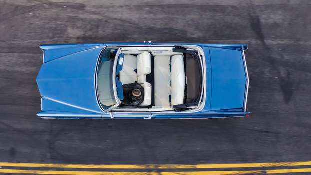 Aerial view of a classic blue convertible car with white interior and a driver in a leather jacket on an asphalt road in Los Angeles California United States. Aerial view of a classic blue convertible car with white interior and a driver in a leather jacket on an asphalt road in Los Angeles California United States.
