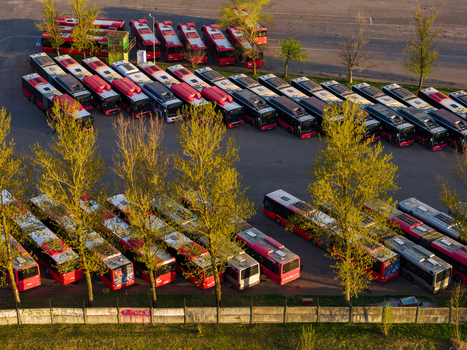 Vilnius County Lithuania 01 May 2026 Aerial view of a bus depot with rows of red and black public transport vehicles parked among green trees during golden hour. Vilnius County Lithuania 01 May 2026 Aerial view of a bus depot with rows of red and black public transport vehicles parked among green trees during golden hour.