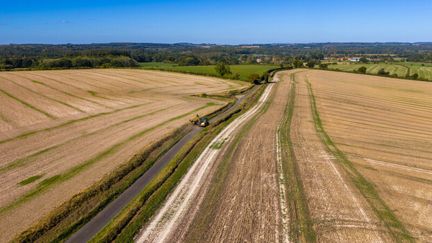 Aerial view of a tractor trimming hedges along a country road through harvested fields at Pepperbox Hill in Salisbury England United Kingdom. Aerial view of a tractor trimming hedges along a country road through harvested fields at Pepperbox Hill in Salisbury England United Kingdom.