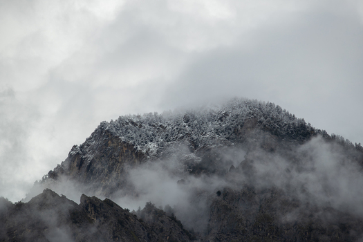 View of a snow dusted mountain peak rising through thick grey clouds and swirling mist in Chilas Gilgit Pakistan. View of a snow dusted mountain peak rising through thick grey clouds and swirling mist in Chilas Gilgit Pakistan.