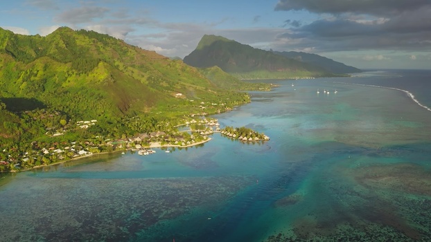 Aerial view of the lush green mountains and turquoise lagoon of Moorea featuring overwater bungalows and boats in the clear water Moorea Maiao Windward Islands French Polynesia. Aerial view of the lush green mountains and turquoise lagoon of Moorea featuring overwater bungalows and boats in the clear water Moorea Maiao Windward Islands French Polynesia.