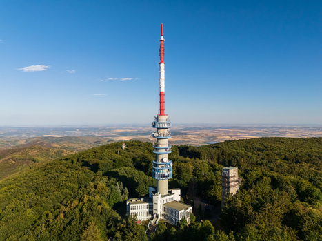 Aerial view of Kekesteto TV Tower in the Matra Mountains Hungary with forested landscape observation deck and telecommunications structures under blue summer sky. Aerial view of Kekesteto TV Tower in the Matra Mountains Hungary with forested landscape observation deck and telecommunications structures under blue summer sky.