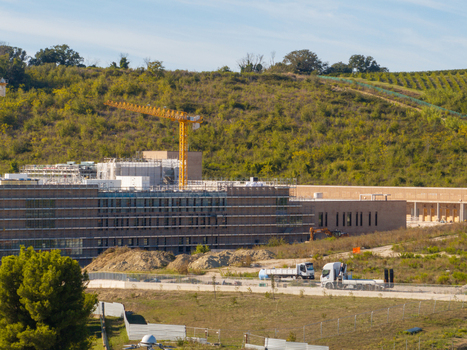 Aerial view of a construction site featuring an Hospital large building under development with a yellow crane scaffolding and heavy machinery in a rural landscape Ancona Marche Italy. Aerial view of a construction site featuring an Hospital large building under development with a yellow crane scaffolding and heavy machinery in a rural landscape Ancona Marche Italy.