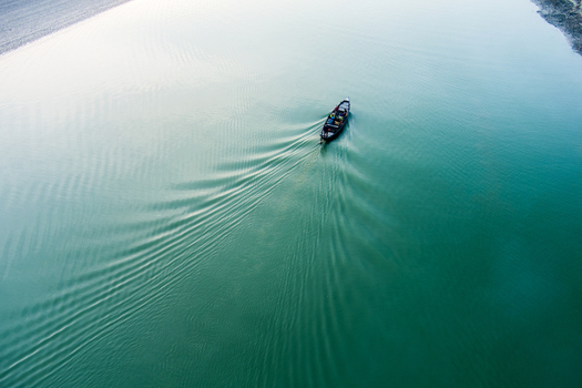 Aerial view of a small boat moving across the calm river creating a wake in Rajshahi Rajshahi Division Bangladesh.