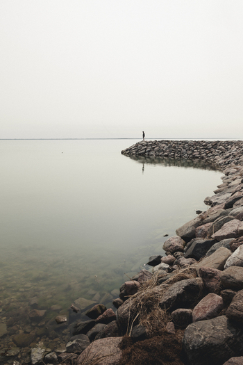 Saxby Laane maakond Estonia 01 June 2025 View of a person standing on the rocky breakwater of Saxby rannik extending into the calm still waters under a soft overcast sky.