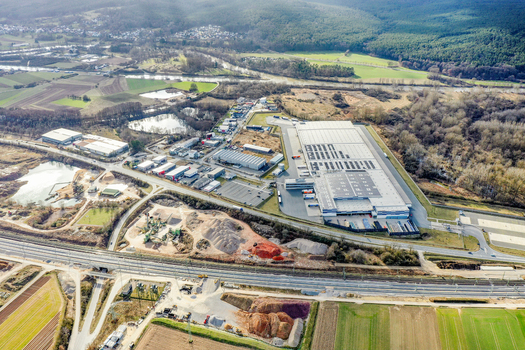 Aerial view of a large industrial logistics center with warehouses and solar panels near a highway and forested hills in Forchheim Bavaria Germany. Aerial view of a large industrial logistics center with warehouses and solar panels near a highway and forested hills in Forchheim Bavaria Germany.
