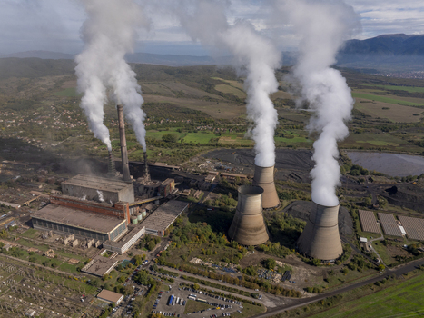 Aerial view of a large coal fired power plant with massive cooling towers emitting thick plumes of steam into the sky set within a rural landscape in Bulgaria.