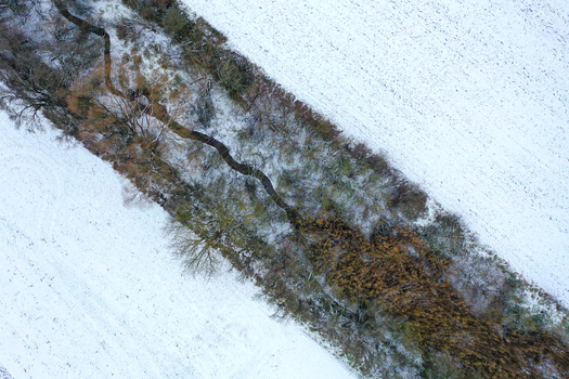 Aerial view of a narrow winding stream flowing through snow covered fields and bare winter trees in Forchheim Bavaria Germany.