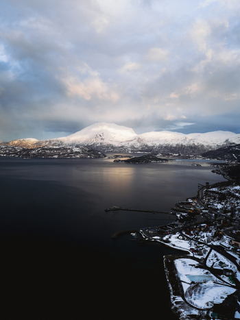Aerial view of the serene waters reflecting the soft glow of the sun near snow capped mountains a landscape of tranquil beauty Sjøvegan Troms Norway. Aerial view of the serene waters reflecting the soft glow of the sun near snow capped mountains a landscape of tranquil beauty Sjøvegan Troms Norway.
